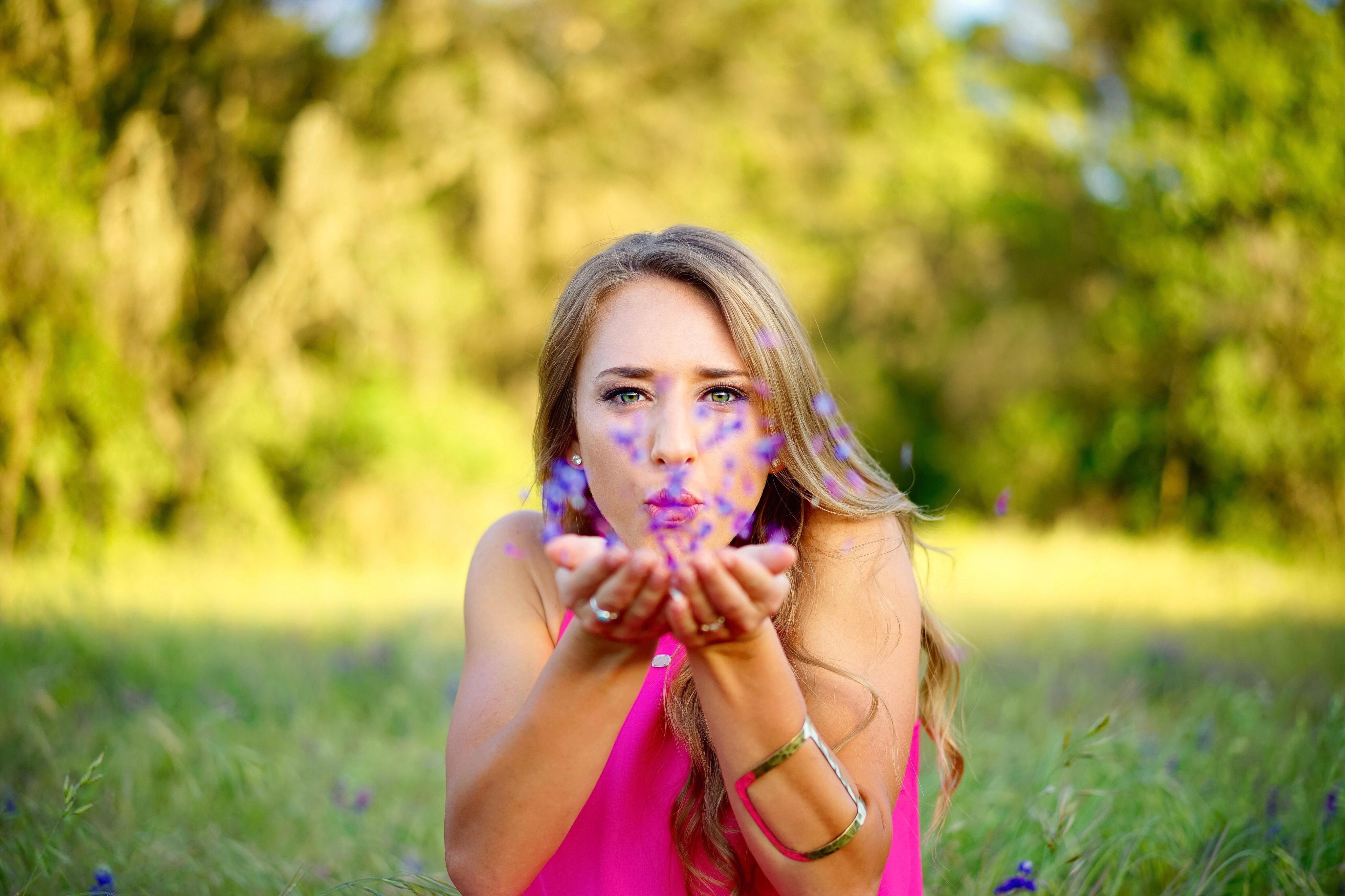 woman in pink dress and with blonde hair, blowing purple flower pedals off her hands, symbolizing the spiritual power of loving yourself quotes