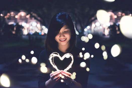 woman holding a string of light in the shape of a heart in front of her face, moving away from abuse towards love