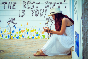 woman sitting in front of a wall painting, the best gift is you, symbolizing how to be a better mom 