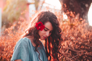 woman with brown hair and flower in hair, in front of a bush in fall, enjoying her divine feminine energy