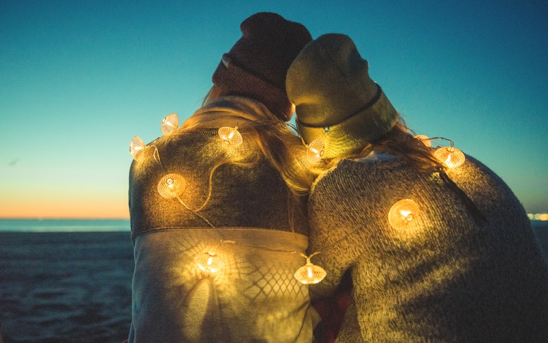 a couple sitting on the beach, with a string of little lights around their back, the opposite of passive aggressive behavior