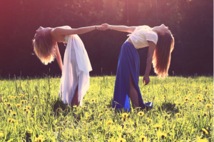 two women in Sommer dresses, dancing in a field of wild flowers, divine feminine energy