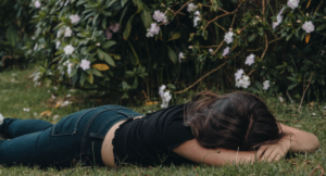 woman laying on the grass in front of flower bushes, being vulnerable shows your most beautiful self